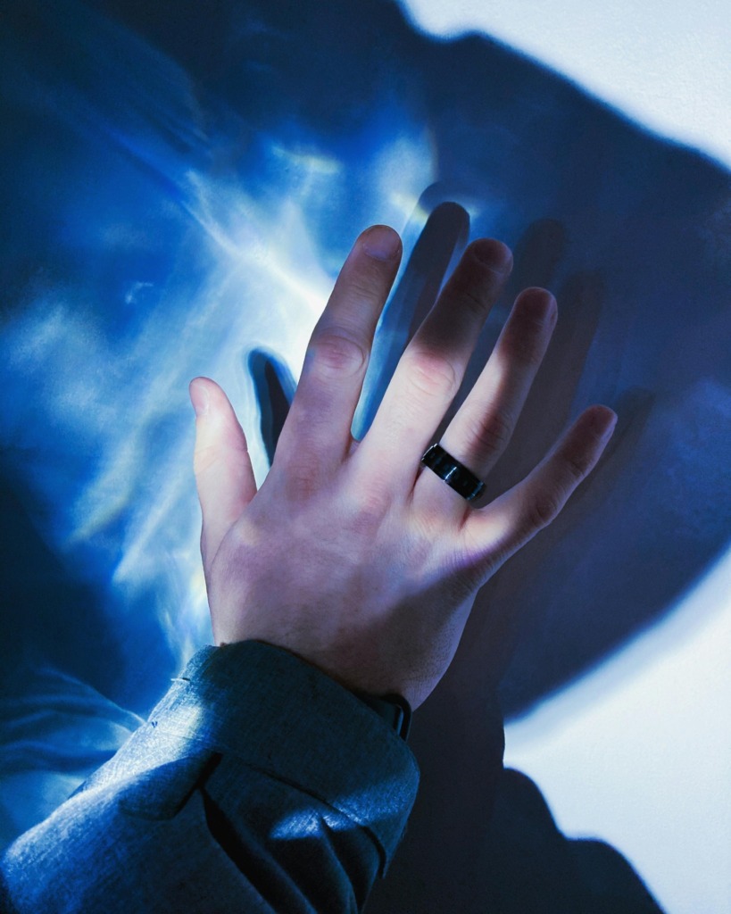 A hand wearing a black ring casts a shadow on a blue abstract background.