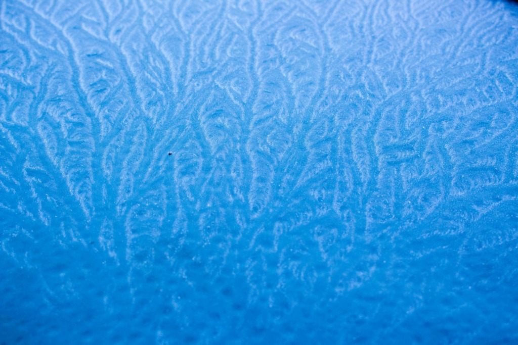 Capture of intricate frost patterns on a blue frozen surface, ideal for abstract backgrounds.